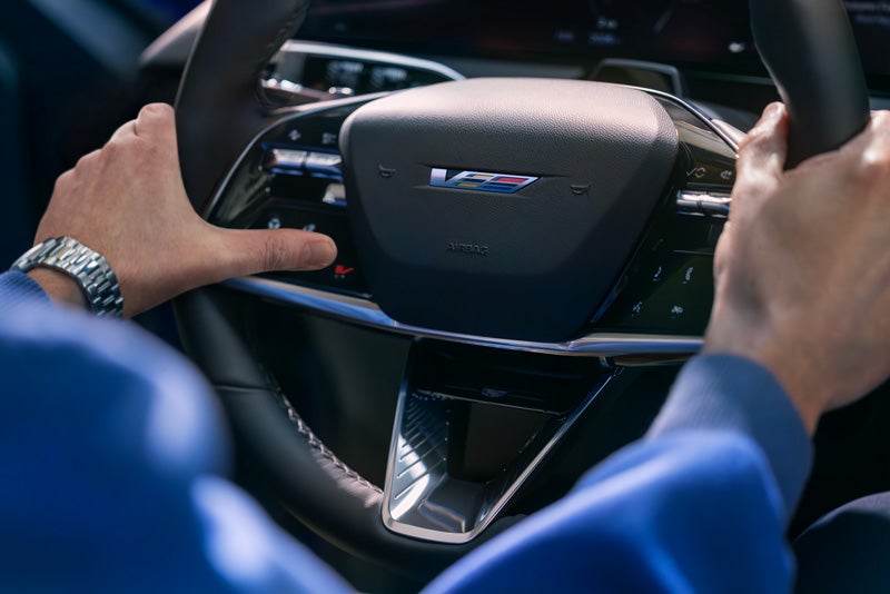 Close-up of a Man About to Press the V-Button on the 2026 OPTIQ-V Steering Wheel | Les Stanford Cadillac in Dearborn MI